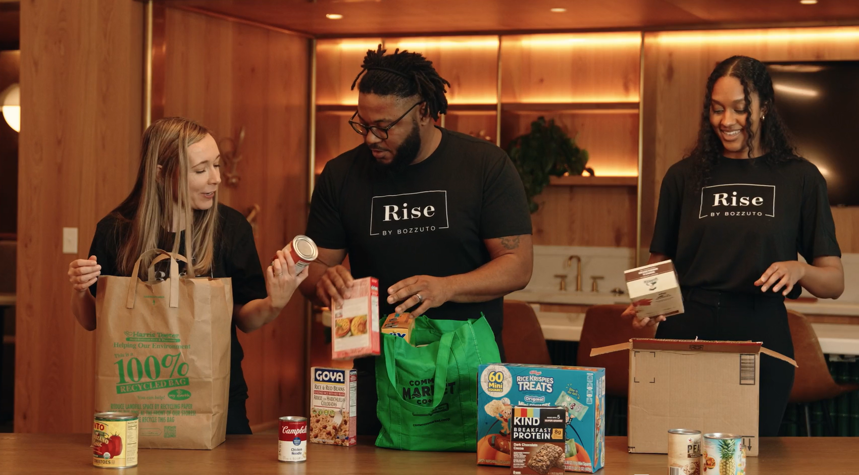 Three people organizing food items on a table in a community space.