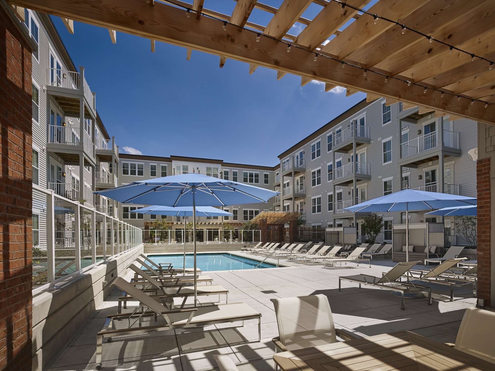 Pool area surrounded by lounge chairs and blue umbrellas at an apartment complex.