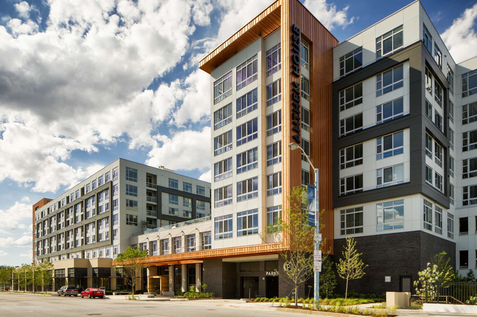 Modern multi-story building with large windows and a wooden facade under a cloudy sky.