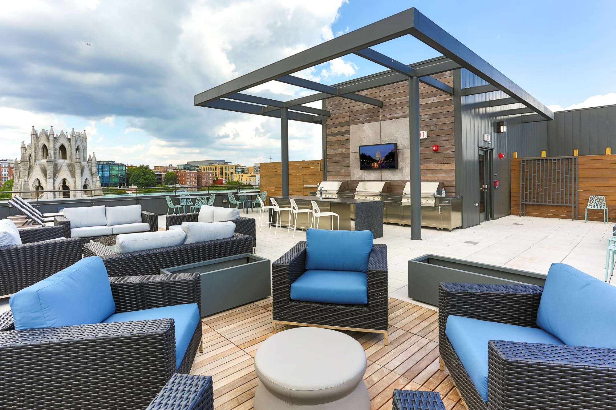 Rooftop patio with seating, barbecue area, and a city view under a blue sky.
