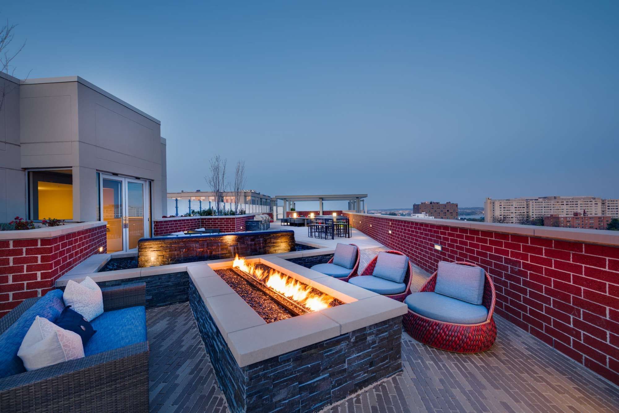 Rooftop lounge area with a fire pit and contemporary seating at dusk.