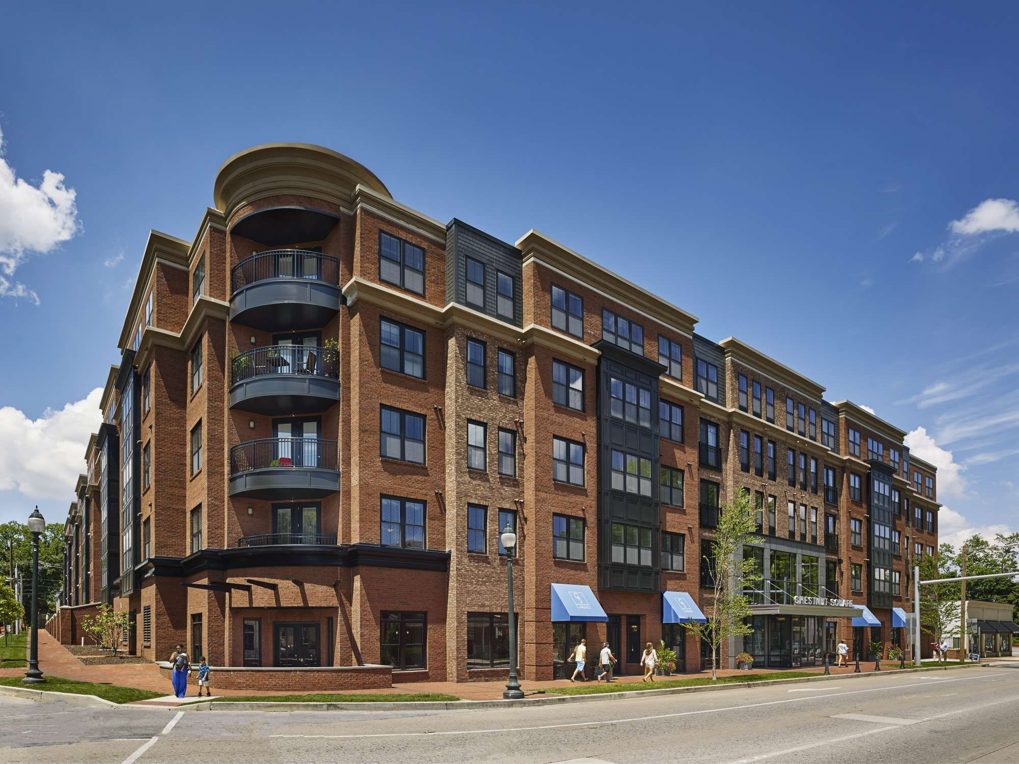 Modern brick apartment building with large windows and blue awnings under a clear sky.