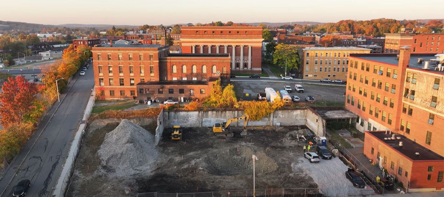 Construction site with a cleared area and buildings in the background, surrounded by autumn trees.