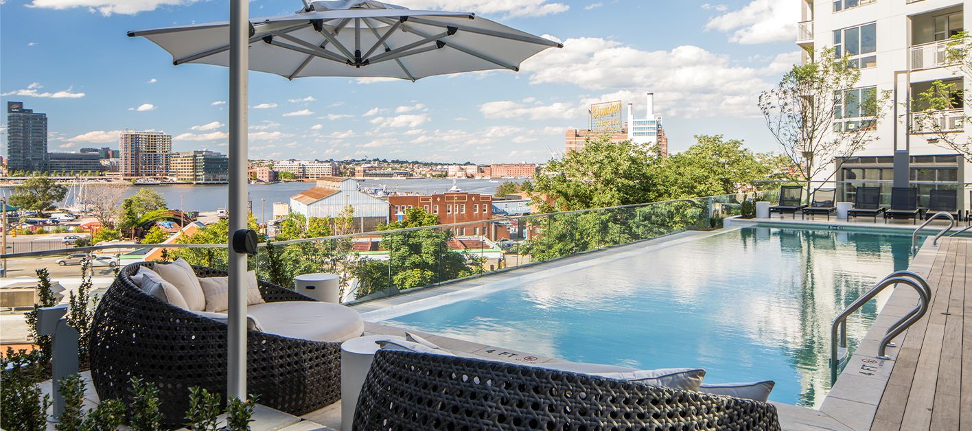 Rooftop pool with lounge chairs and an umbrella overlooking a cityscape.