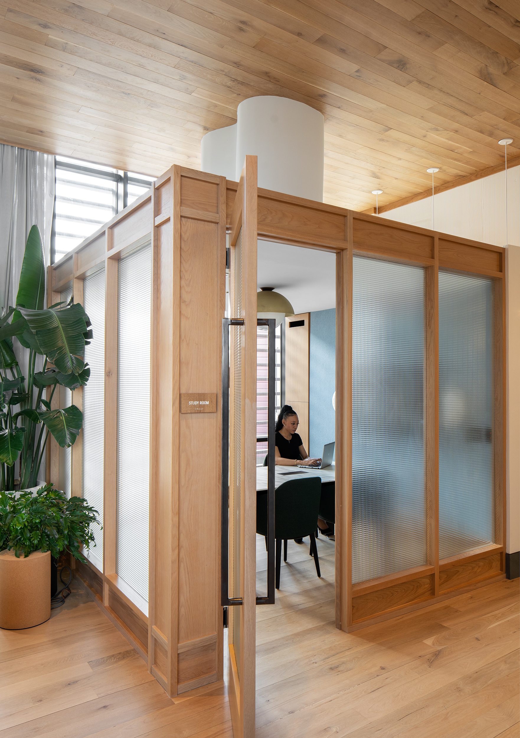 A modern office space with a glass-walled meeting room and a potted plant.