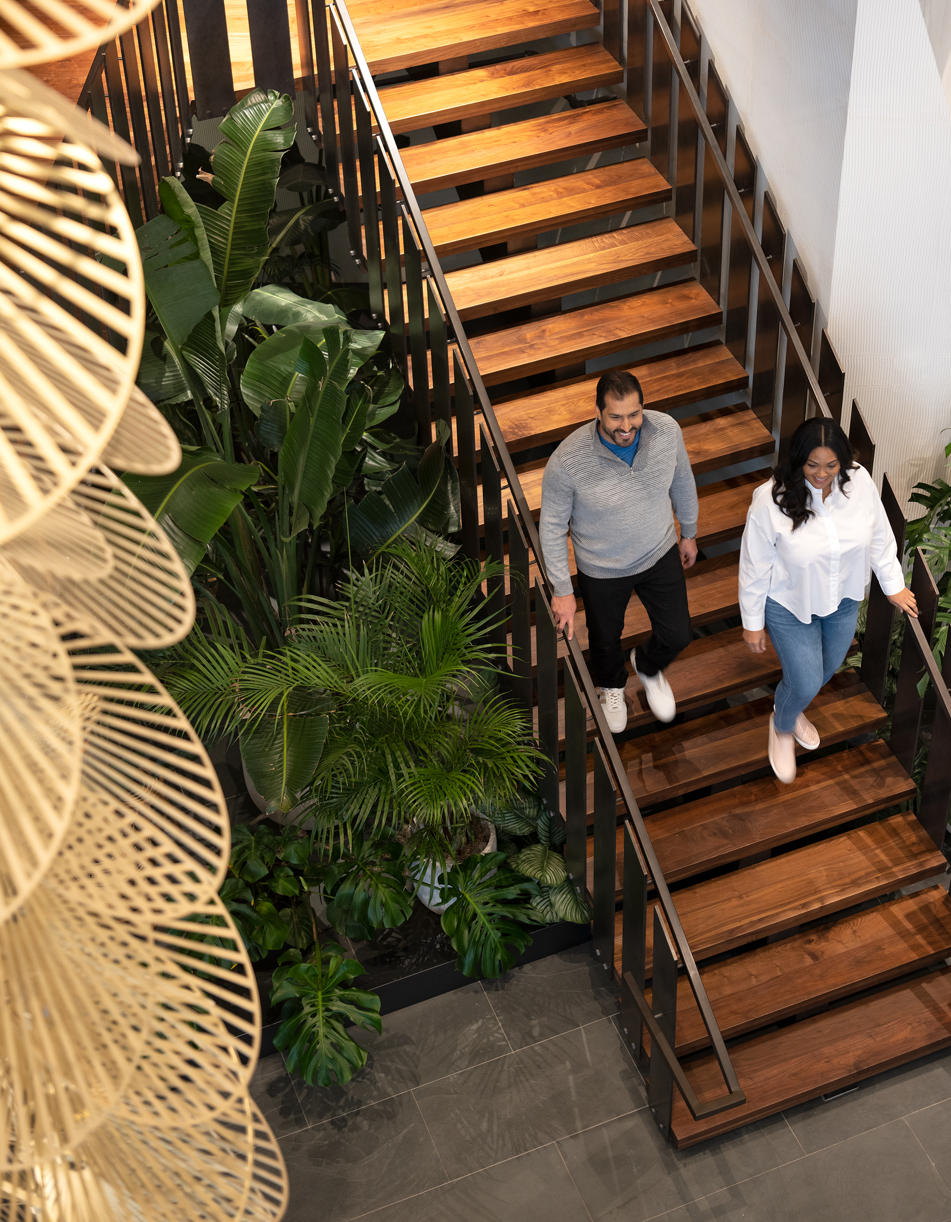 Two people walk down wooden stairs surrounded by greenery.