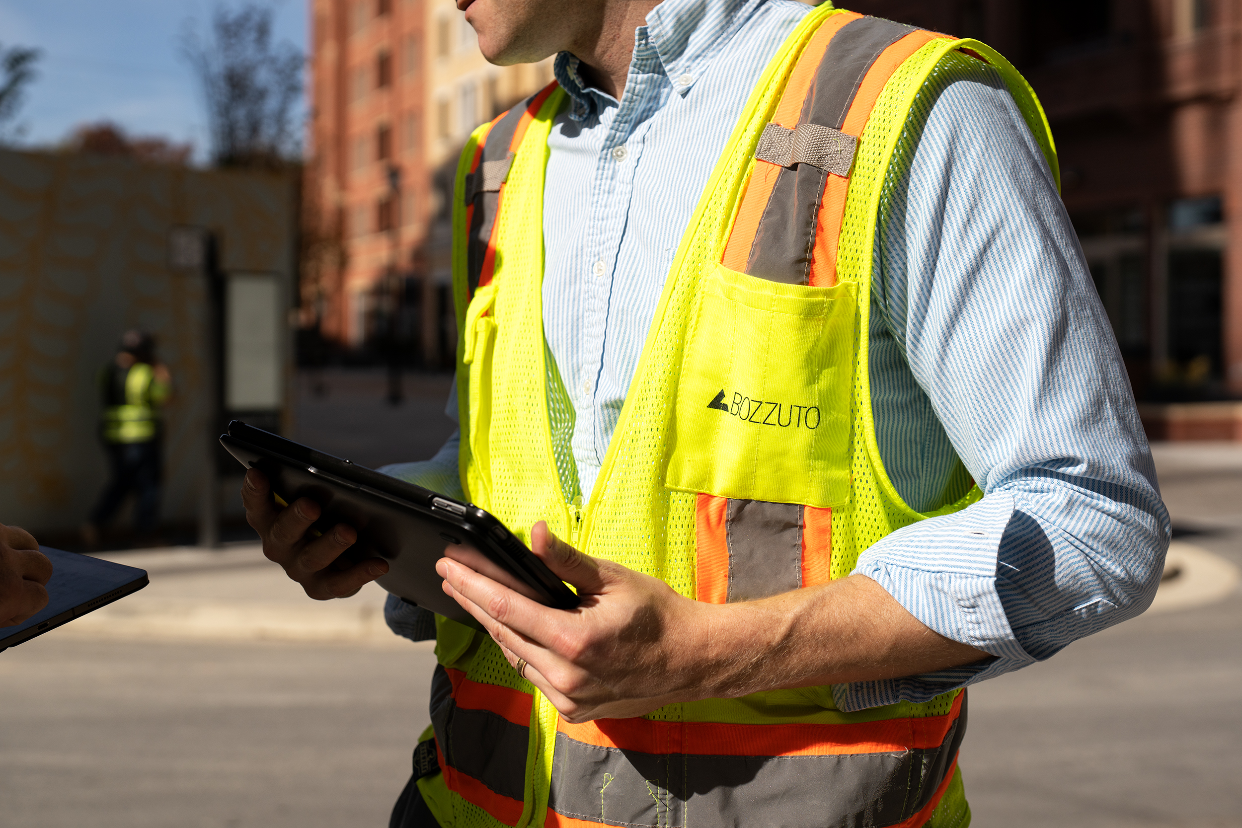 Construction worker in a safety vest using a tablet outdoors.