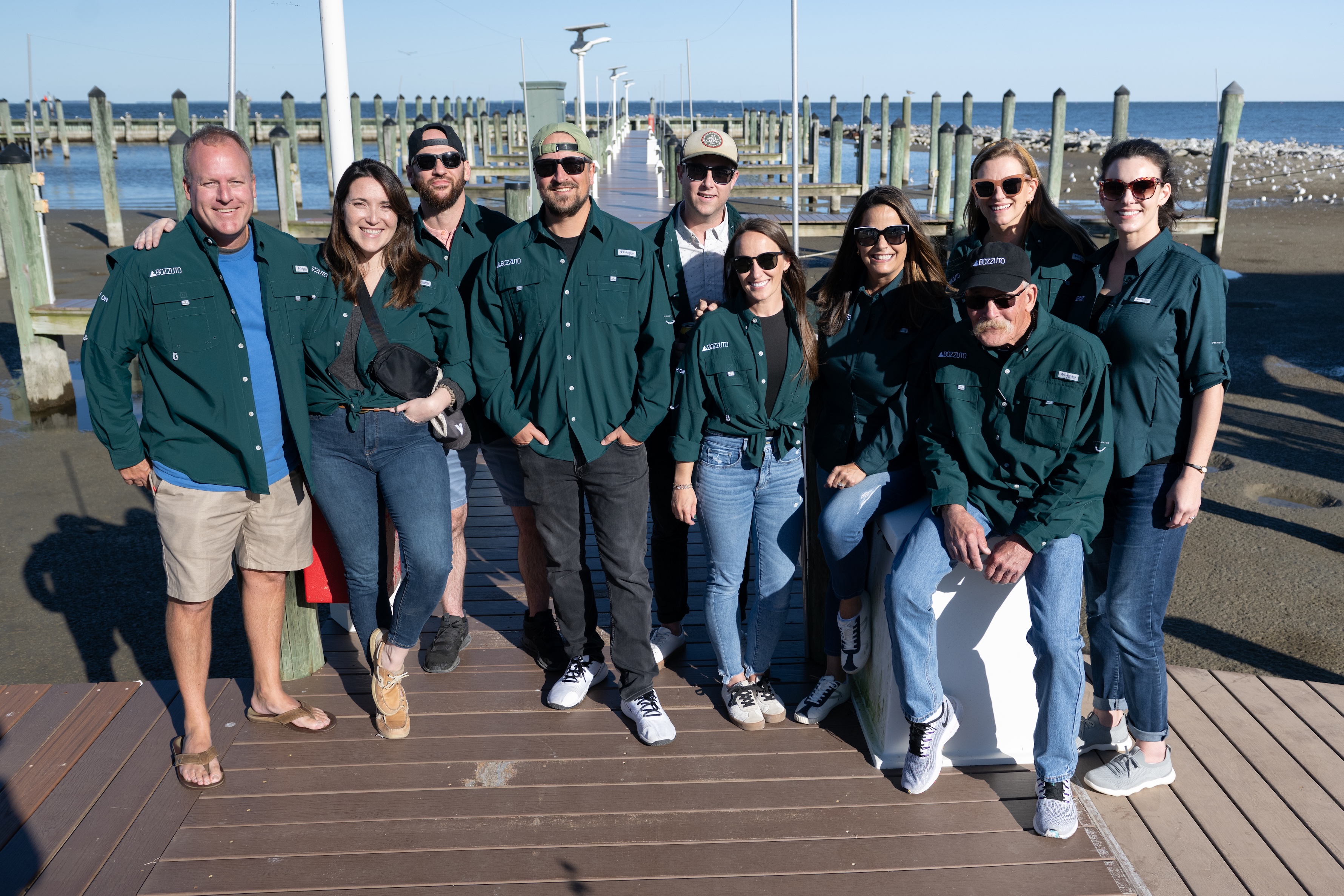 Group of people wearing matching green jackets at a dock.