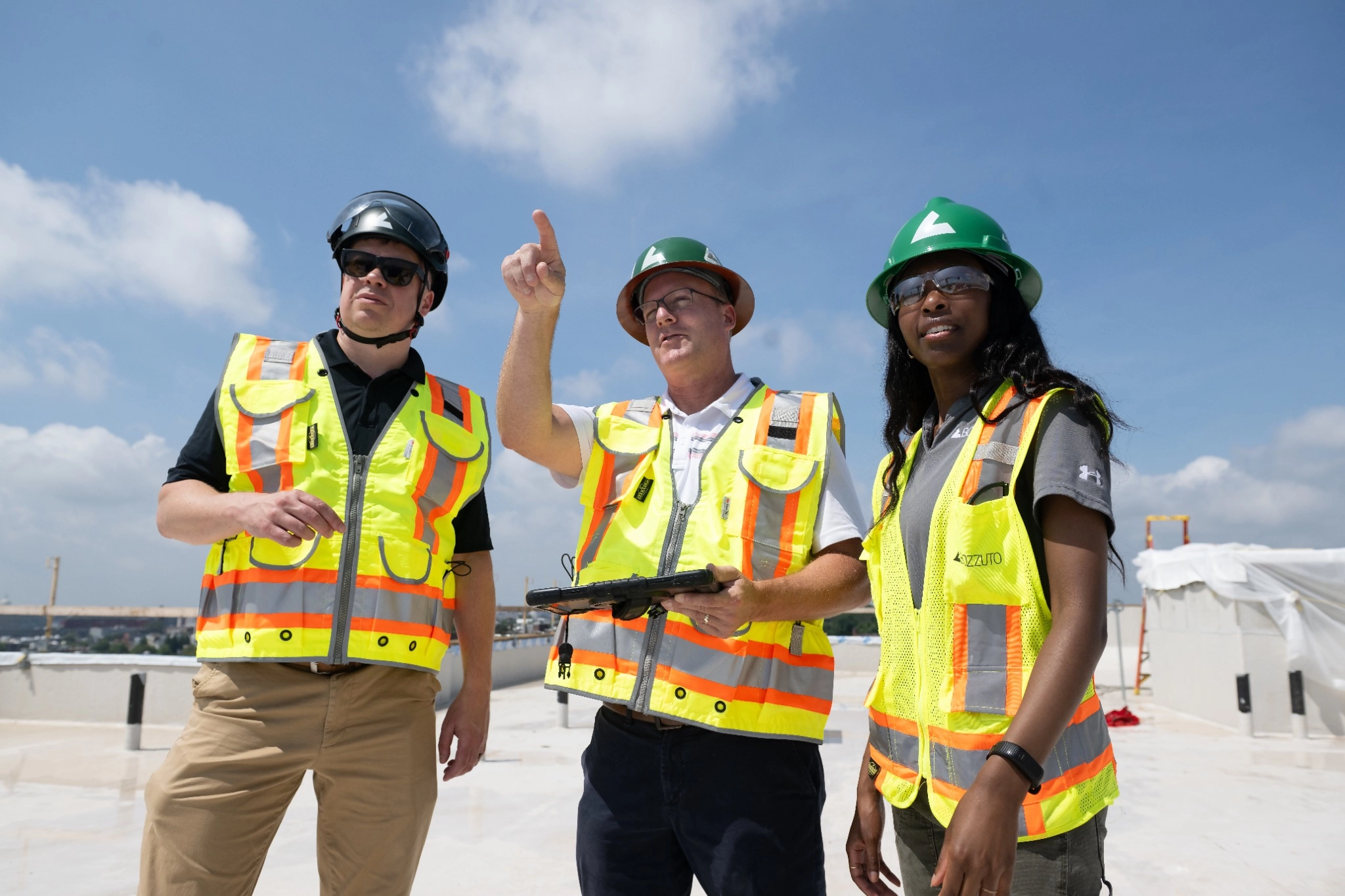 Three construction workers in safety gear discussing site plans.