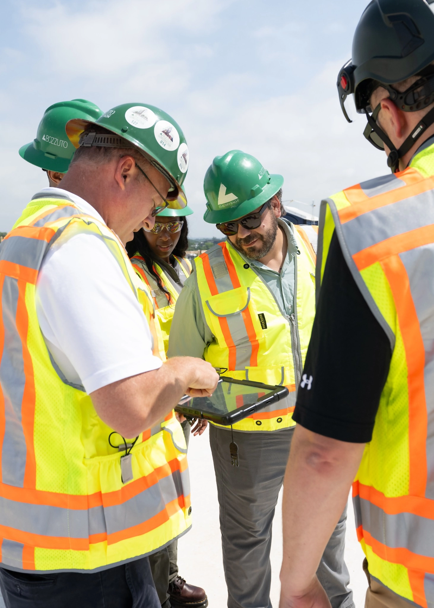 Workers in safety gear examining a tablet outdoors.