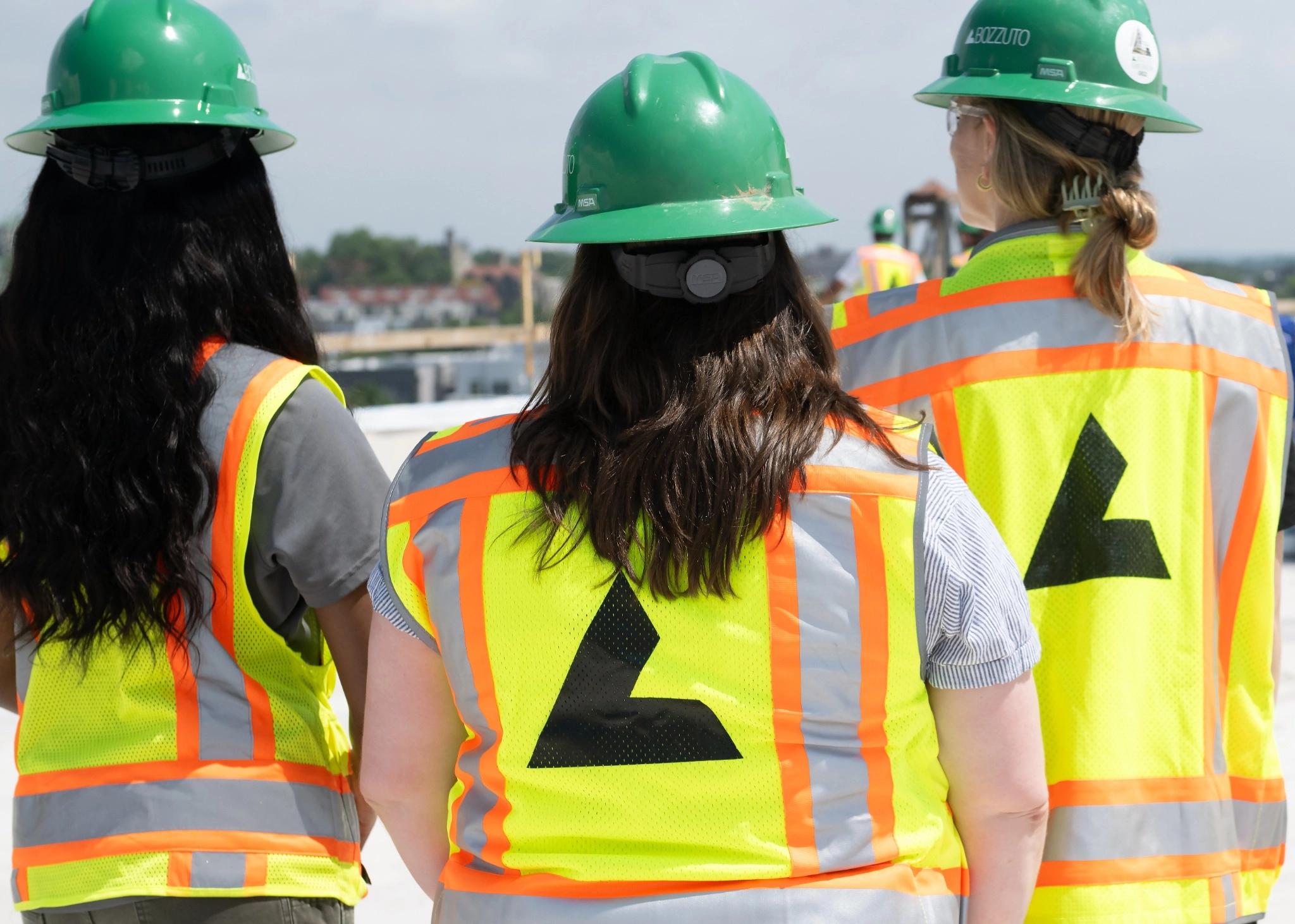 Three women in safety gear with green helmets and reflective vests.