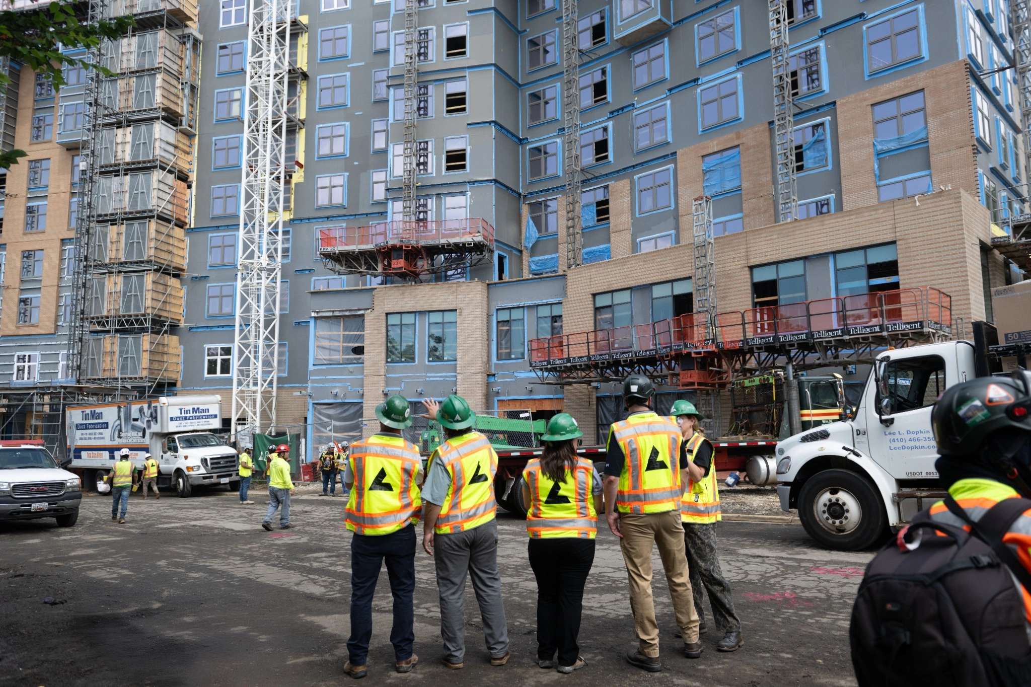 Construction workers in safety gear observe a building site.