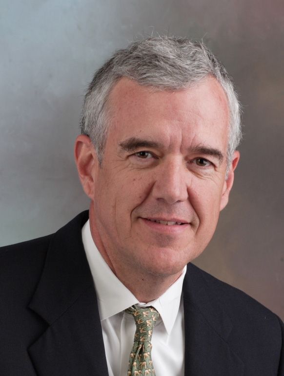 Professional portrait of a man in a suit with gray hair and a neutral background.