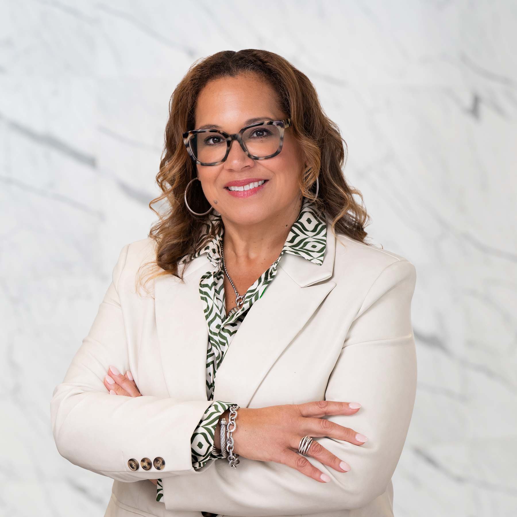A woman in a white blazer stands confidently with arms crossed.