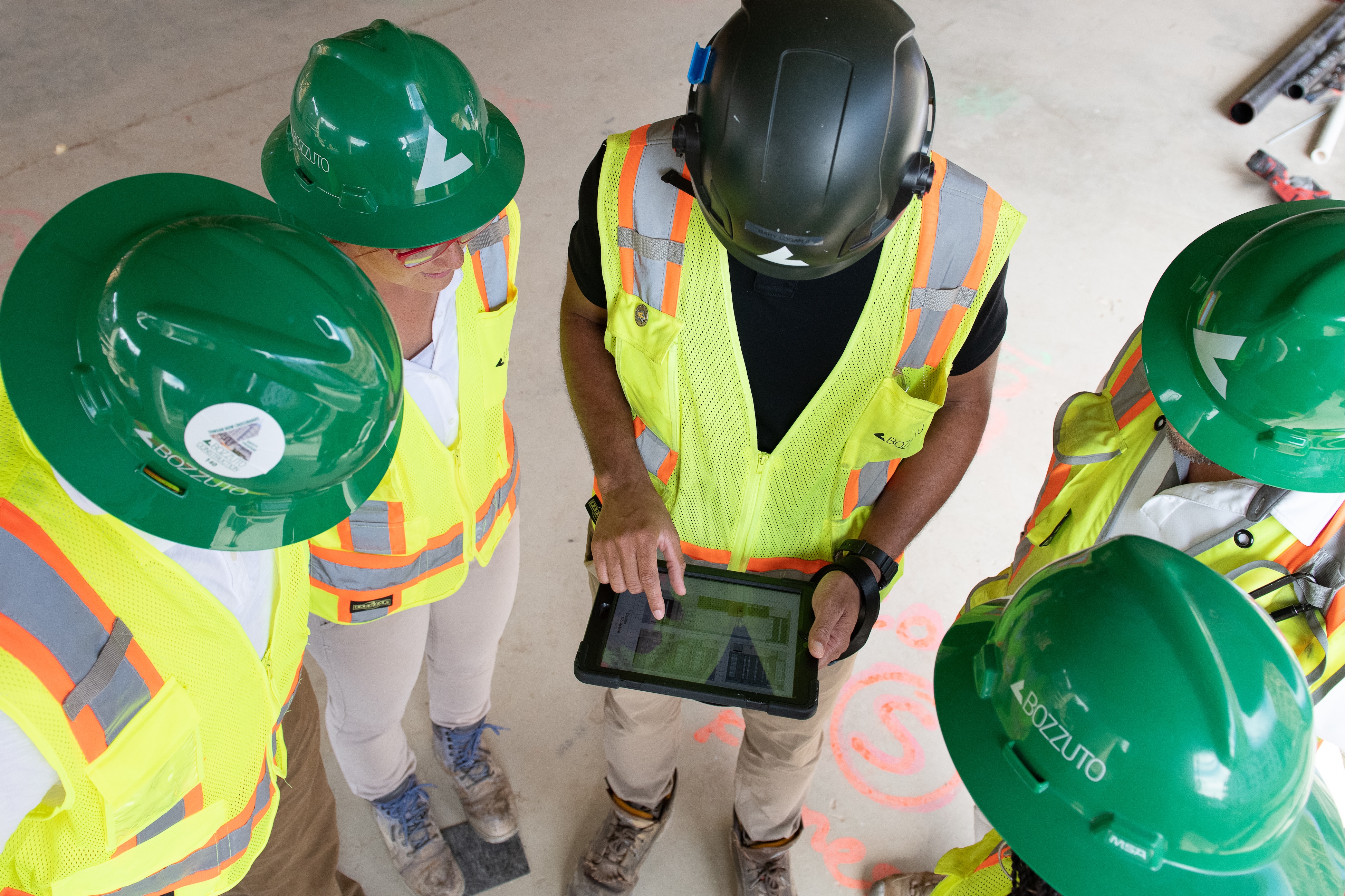 Group of workers in helmets reviewing data on a tablet at a construction site.