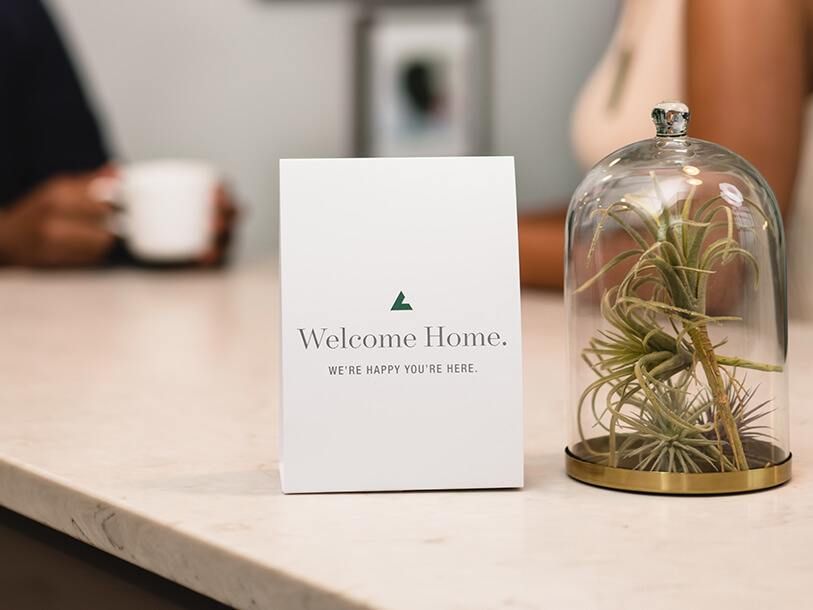 Welcome card on a table with a decorative glass dome and plant.