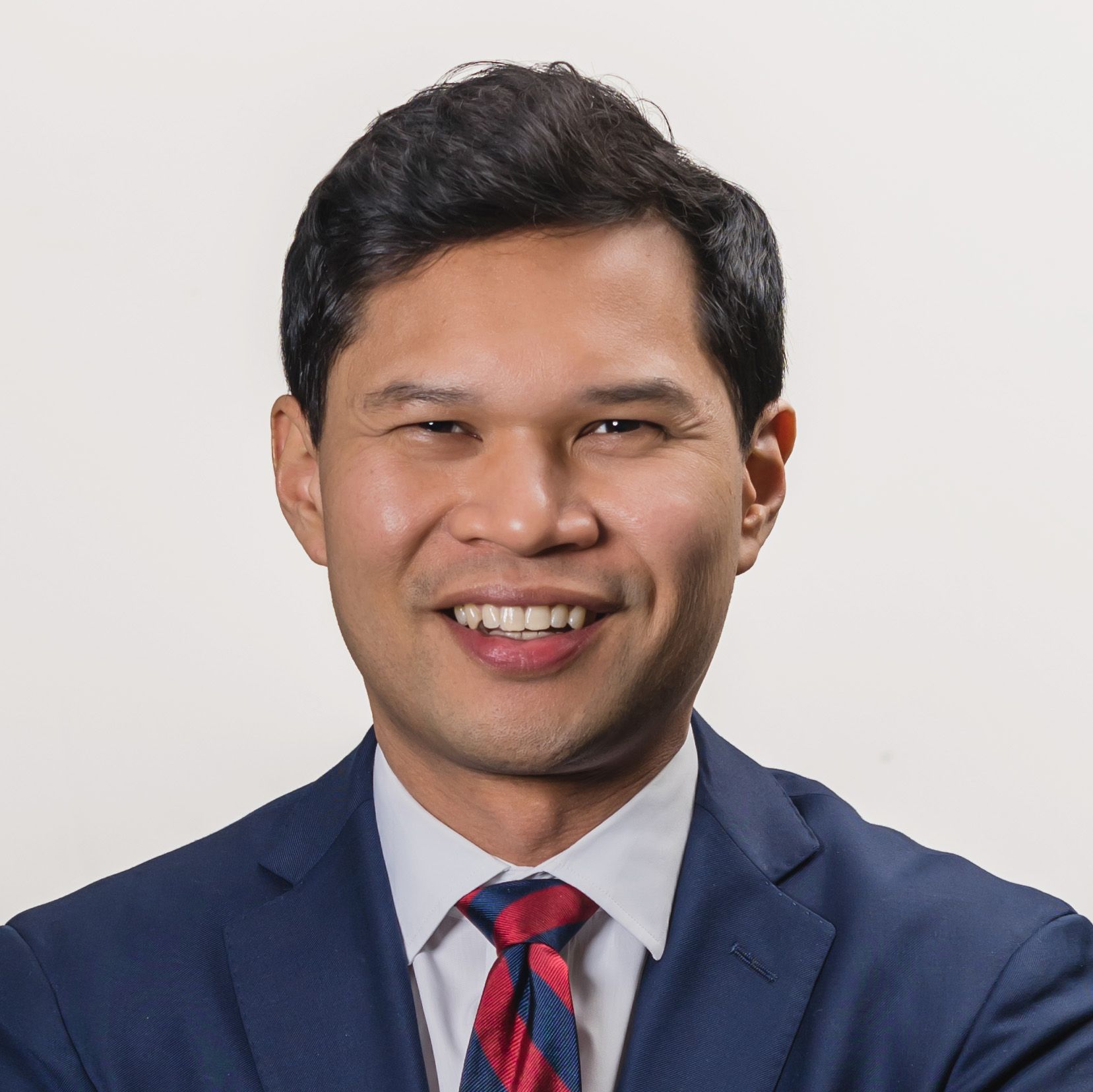 Smiling man in a suit with a striped tie, against a plain background.