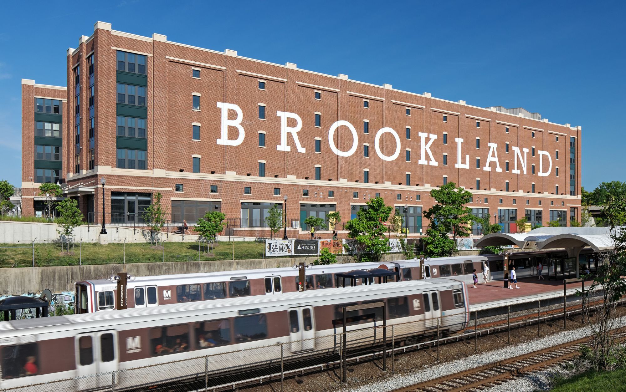 Brown brick building with "BROOKLAND" sign and a nearby train station.