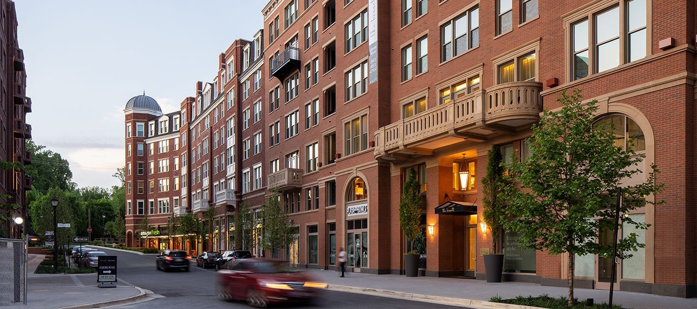 A street view of brick apartment buildings with trees and parked cars at dusk.