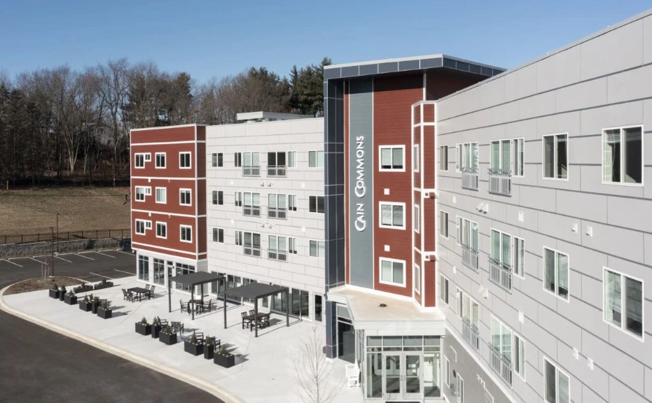 Modern four-story apartment building with a gray and red exterior, featuring large windows and contemporary architectural details