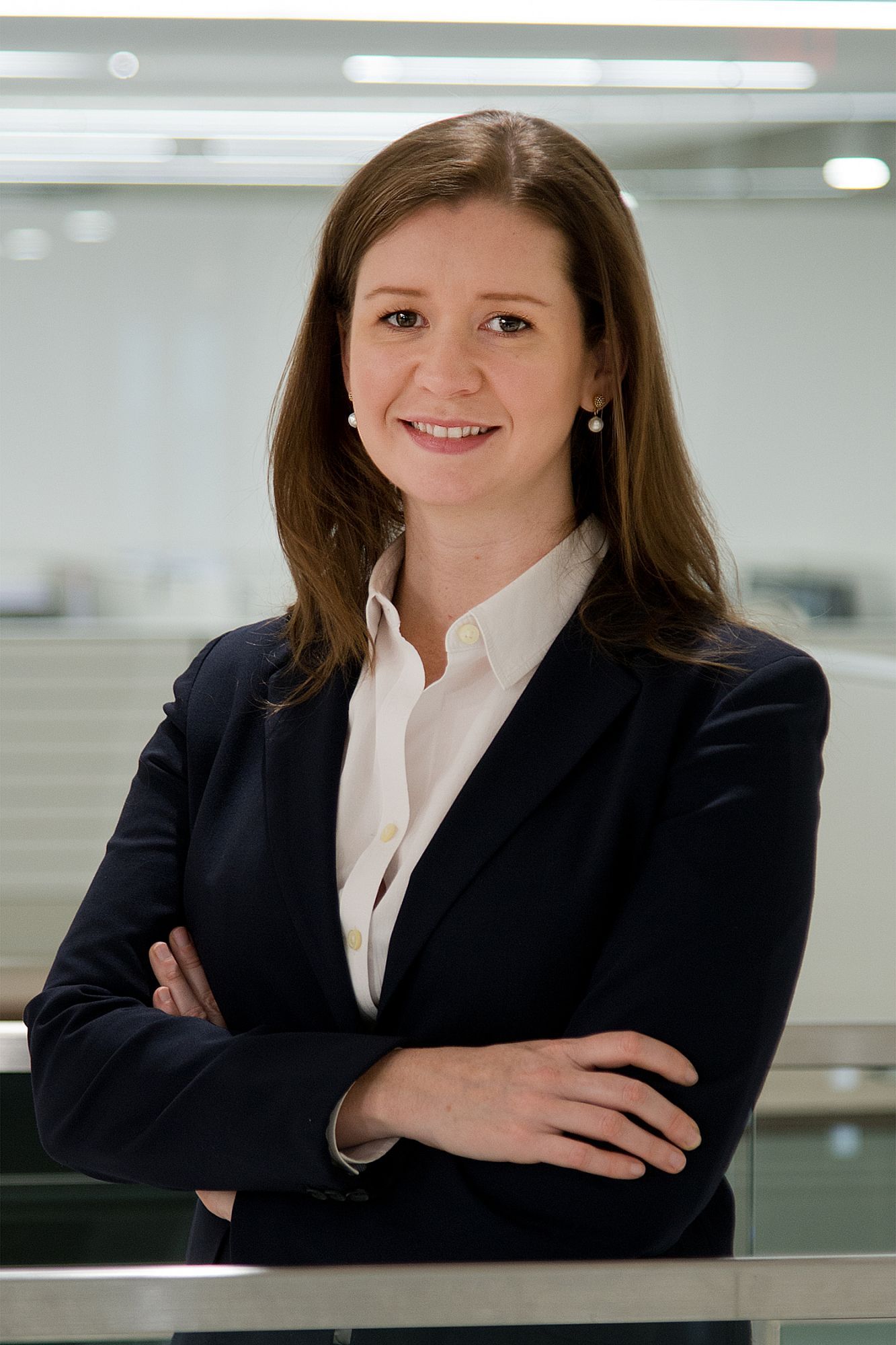 Professional woman in a blazer, smiling with arms crossed in an office setting.