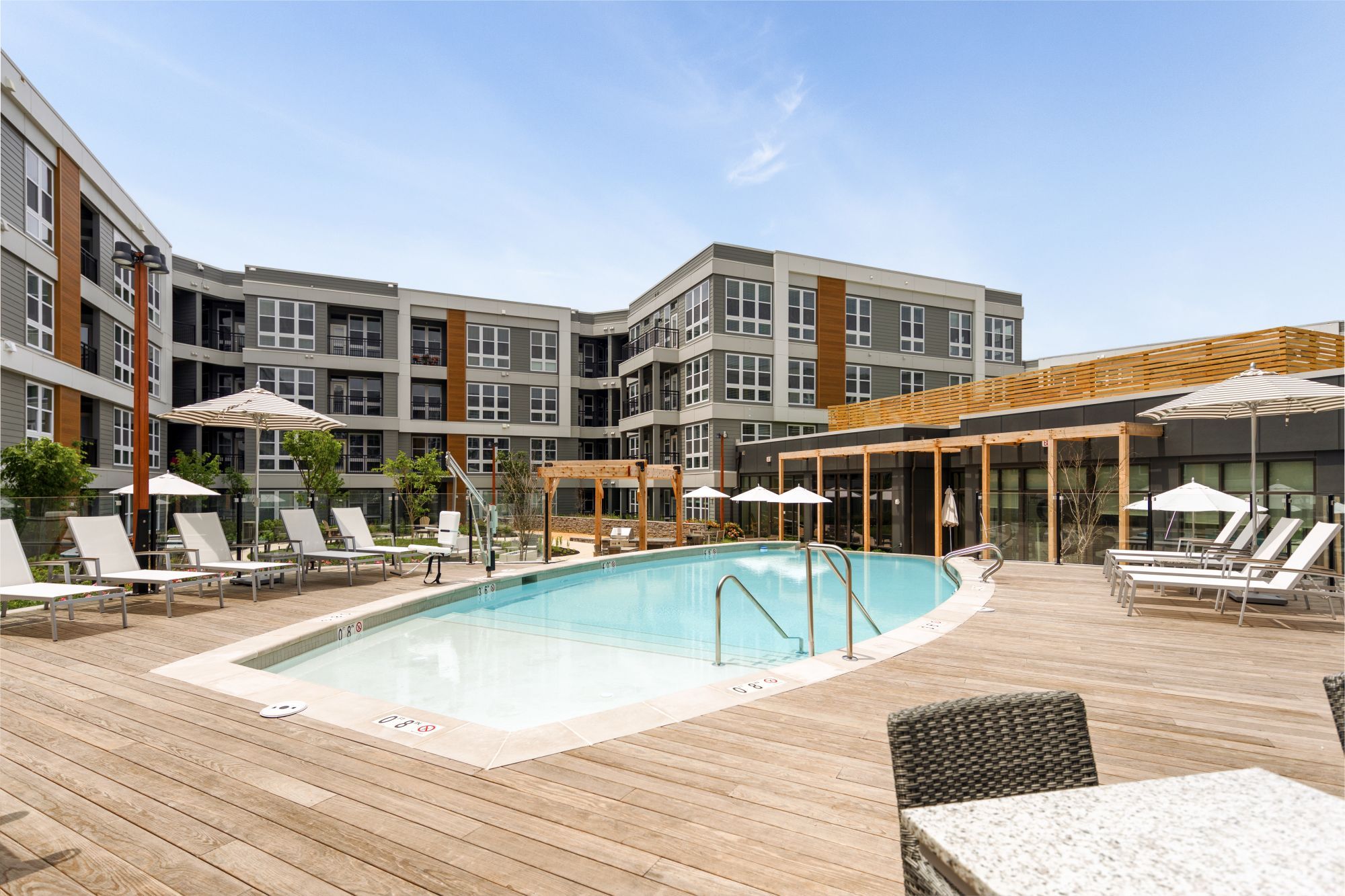 Modern pool area surrounded by lounge chairs and buildings under a clear blue sky.