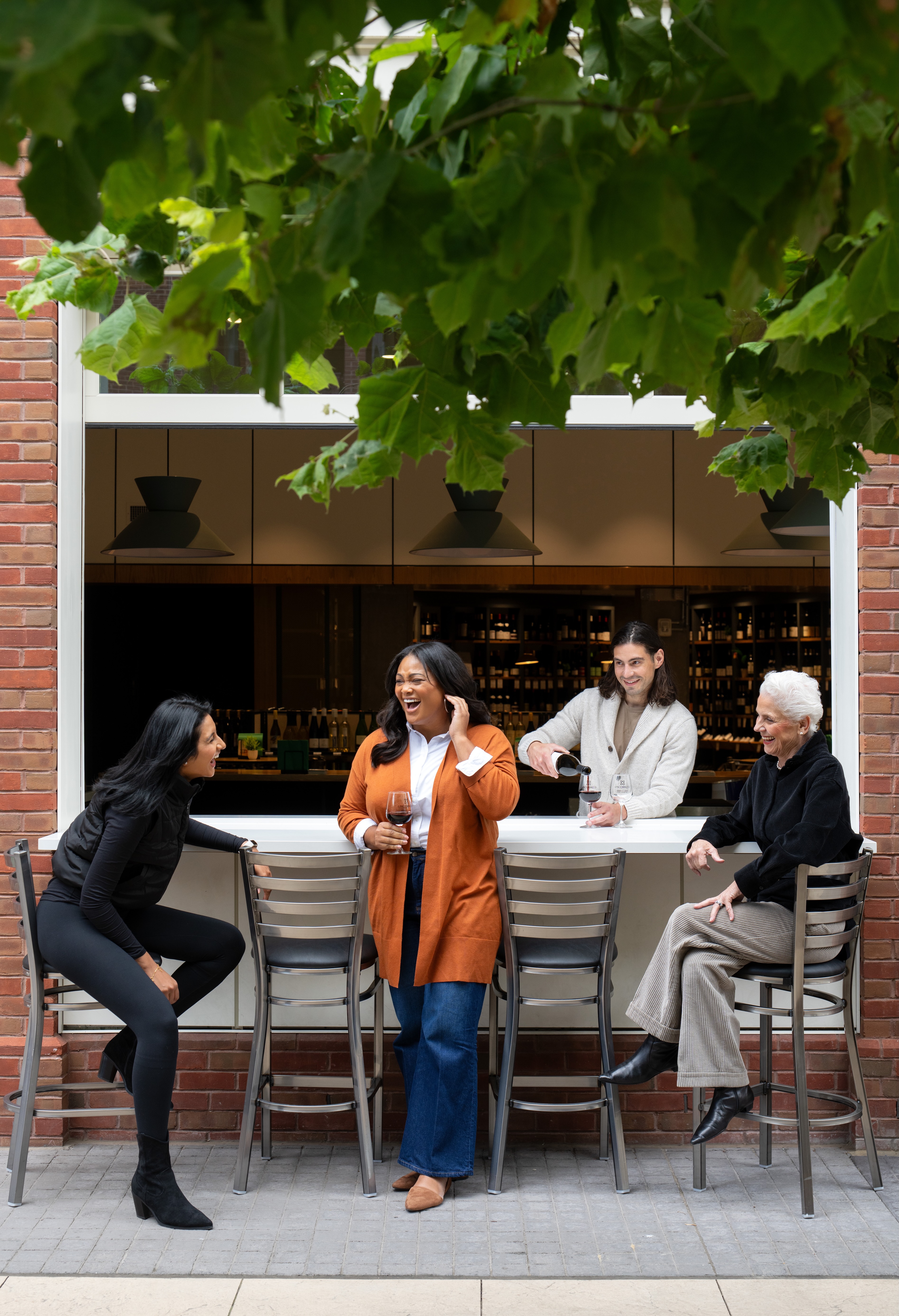 Four women interacting outside a café with a large window.