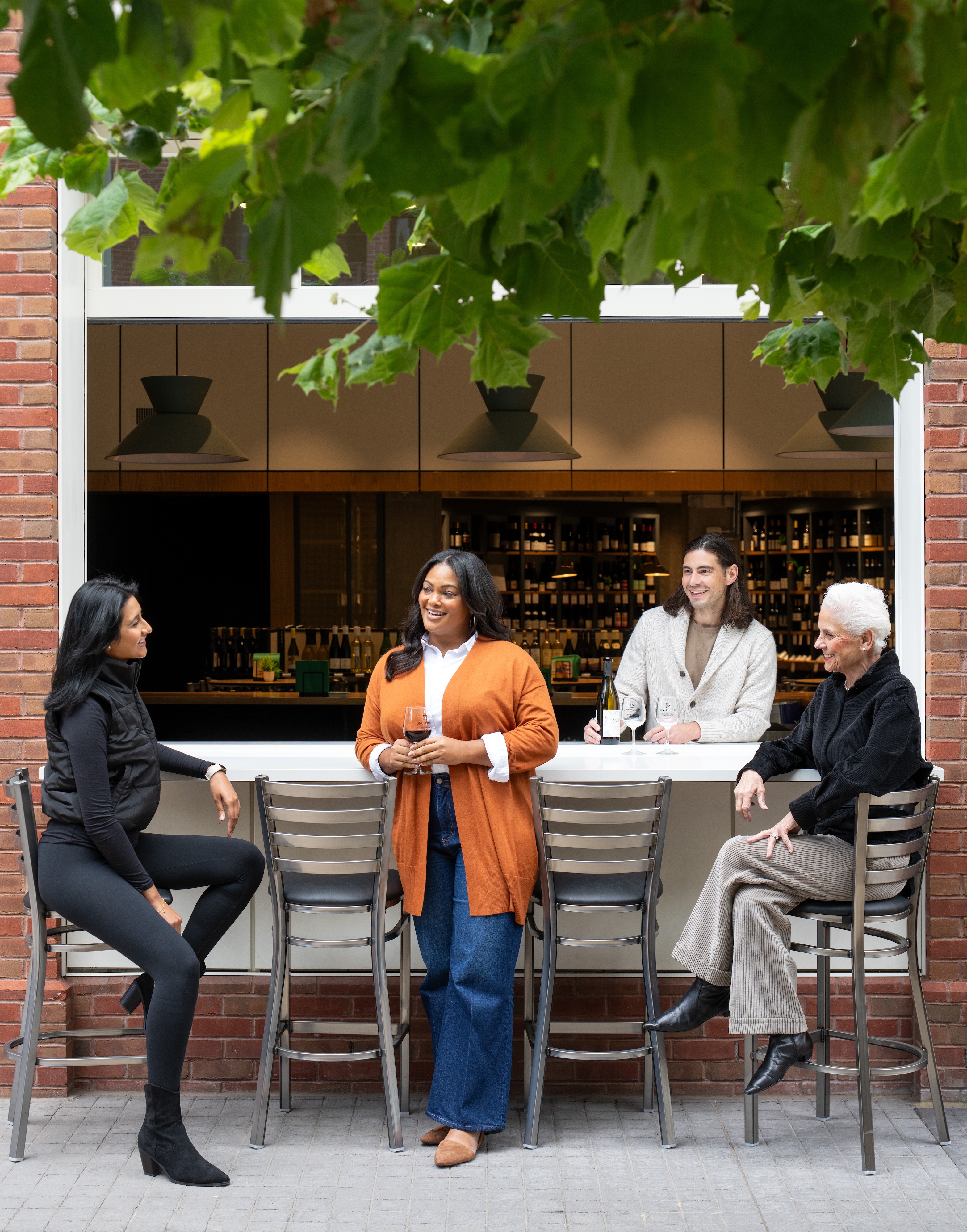 Four people sitting and standing at a bar with a window view.