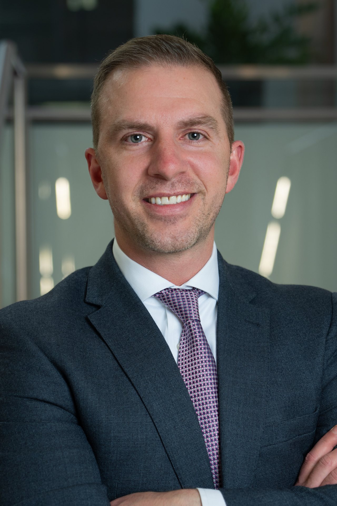 Professional portrait of Collin Hoffmann smiling in a business suit, with a modern office background.