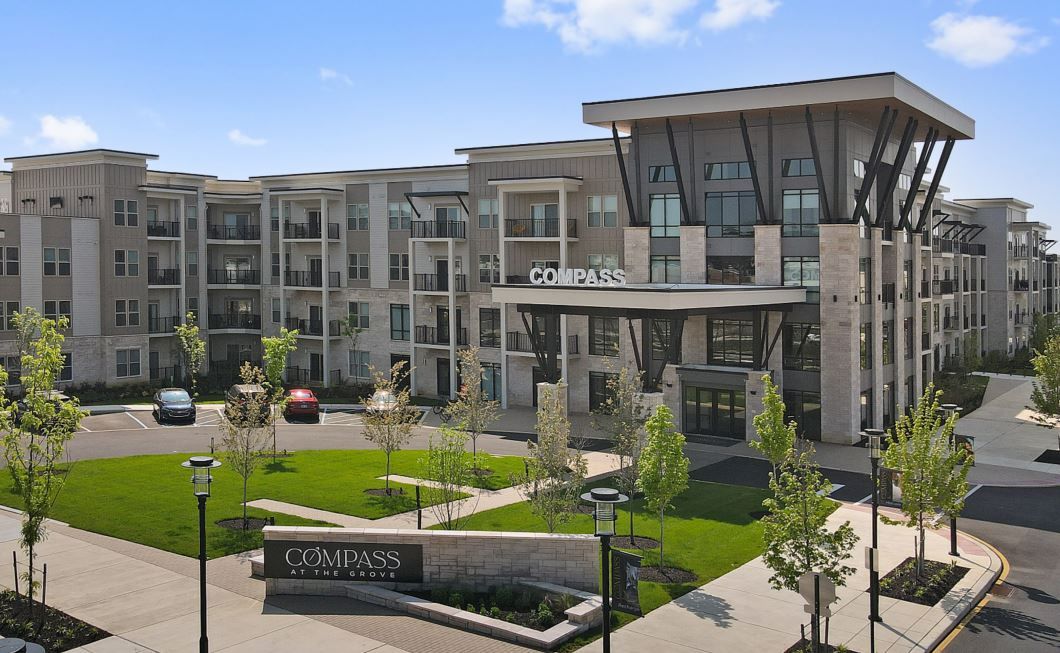Modern apartment building with a landscaped entrance and parking area.