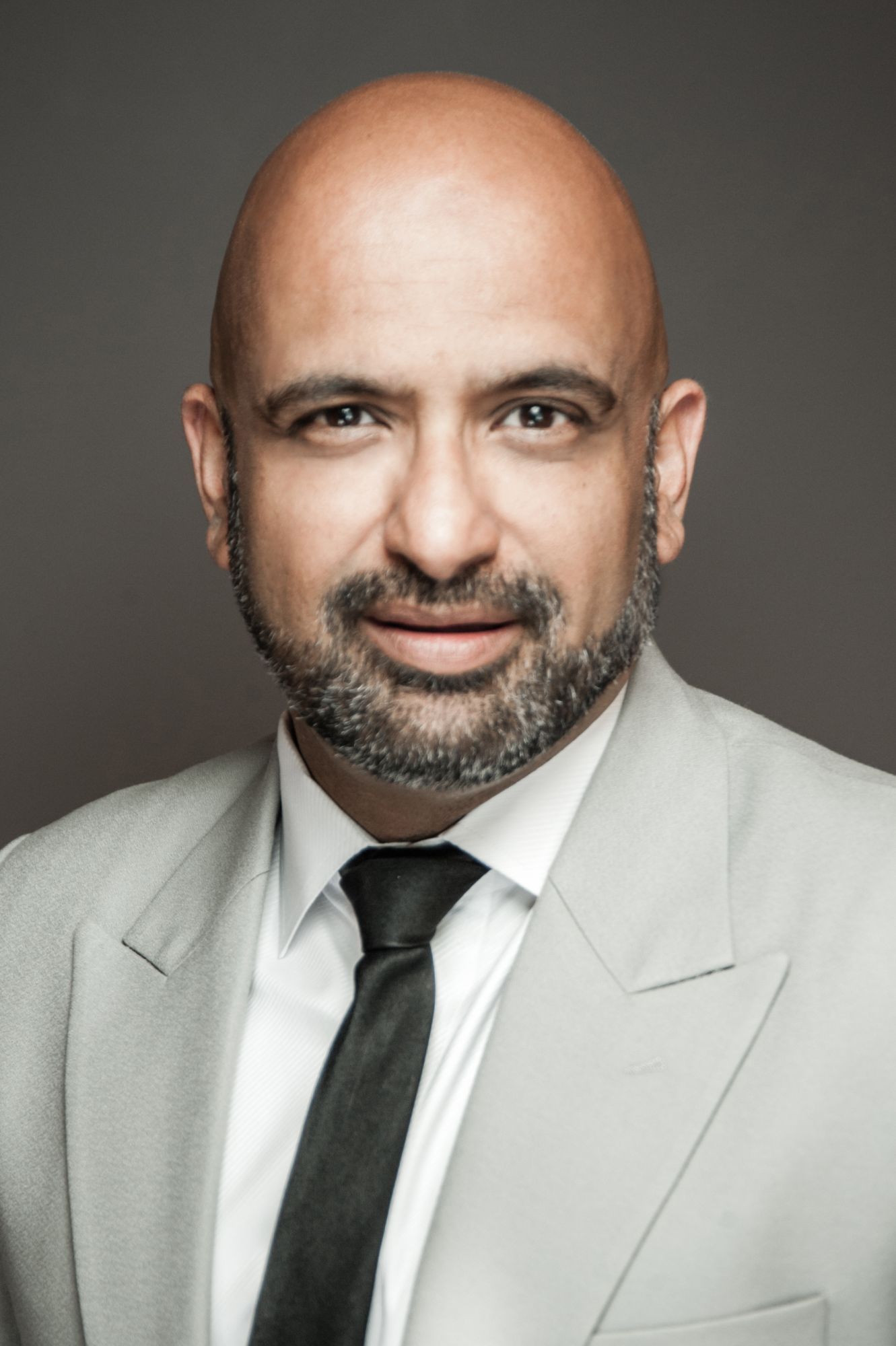 Smiling man in a suit with a bald head against a neutral background.