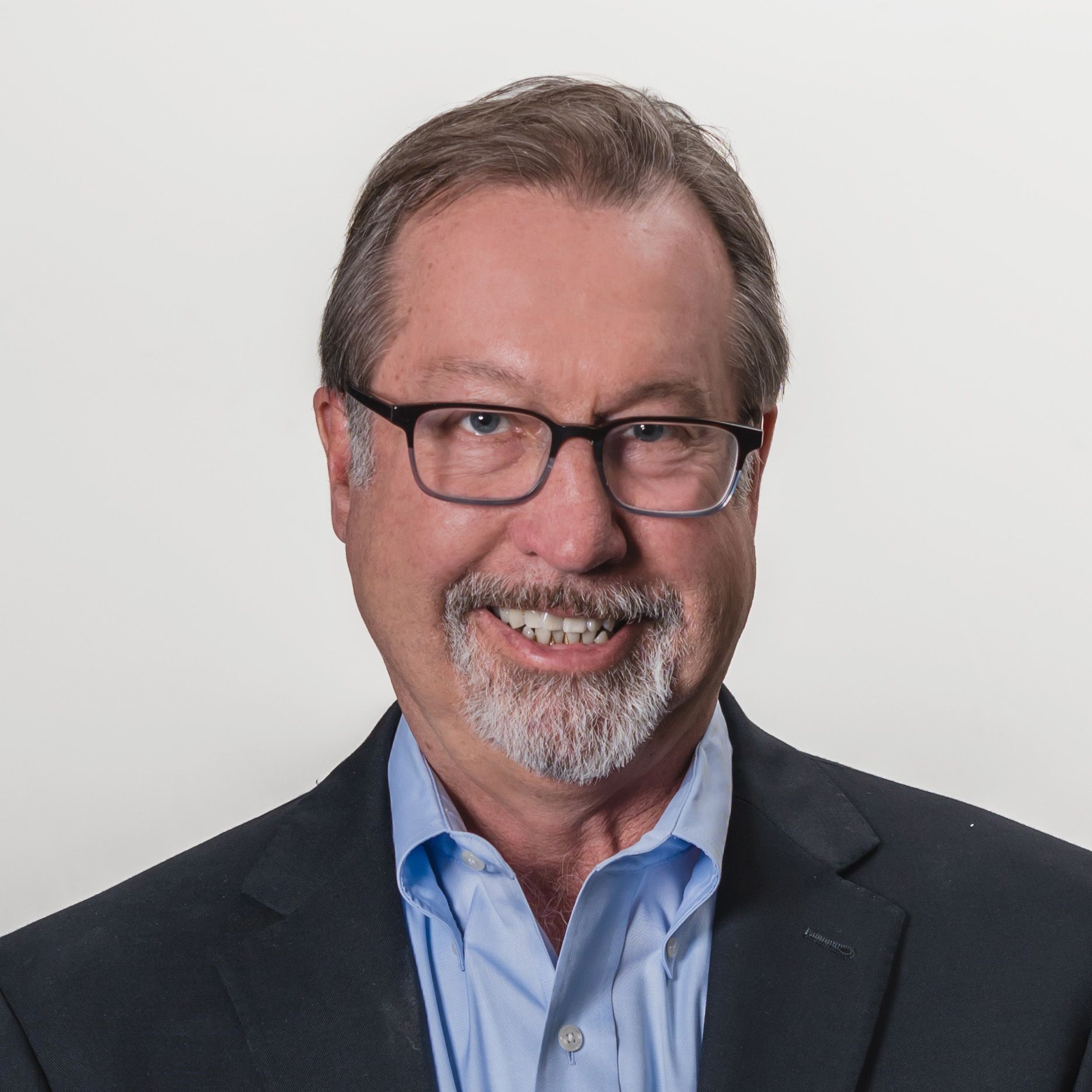 A smiling man with glasses wearing a suit jacket and shirt.