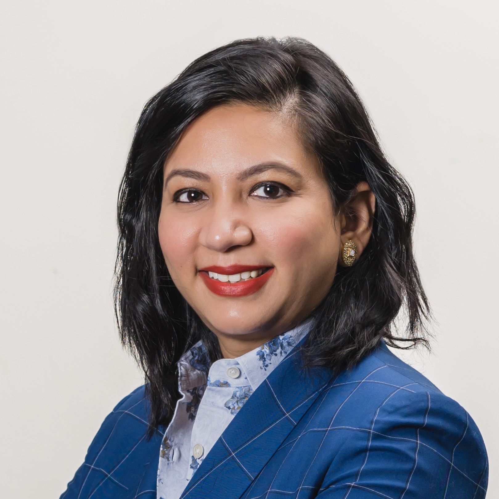 A professional woman smiles, wearing a blue blazer and a patterned blouse.