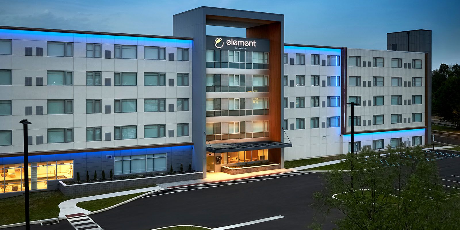 Modern hotel exterior with blue lighting and a landscaped entrance.
