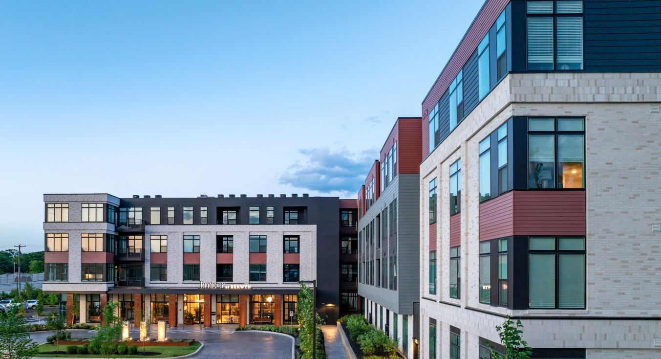 Modern multi-story residential building with landscaped entrance at dusk.