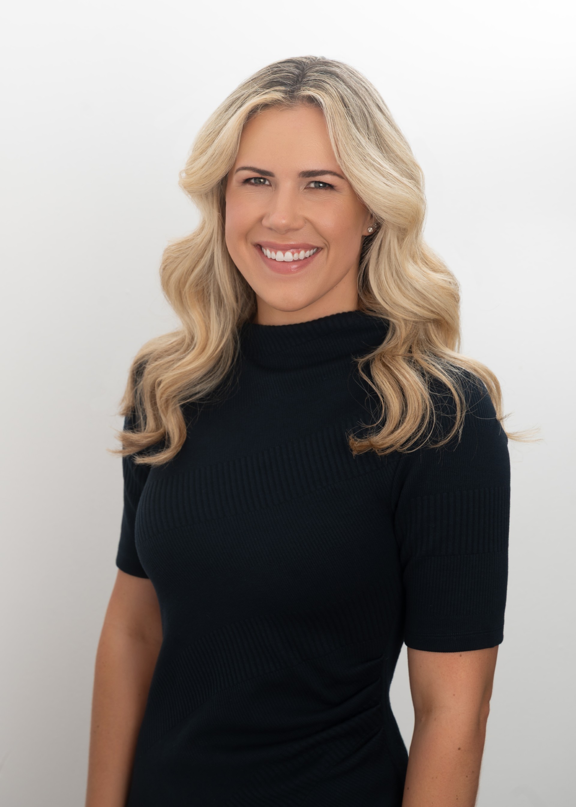 Erin Carney smiles warmly, wearing a black top against a white background.