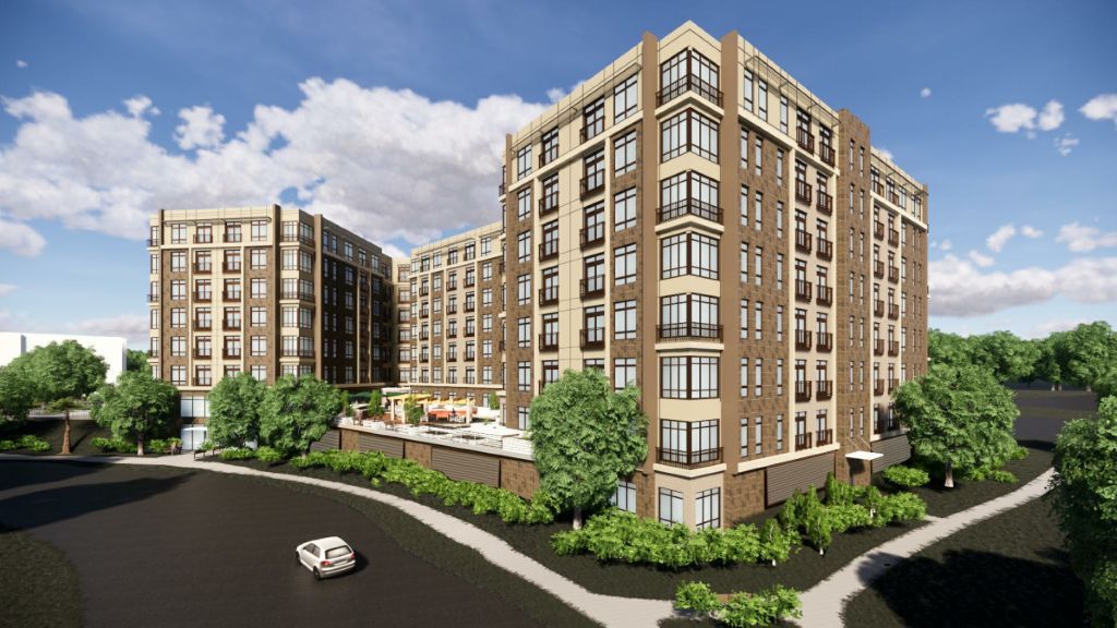 Modern apartment building with multiple stories surrounded by greenery and a parking area.