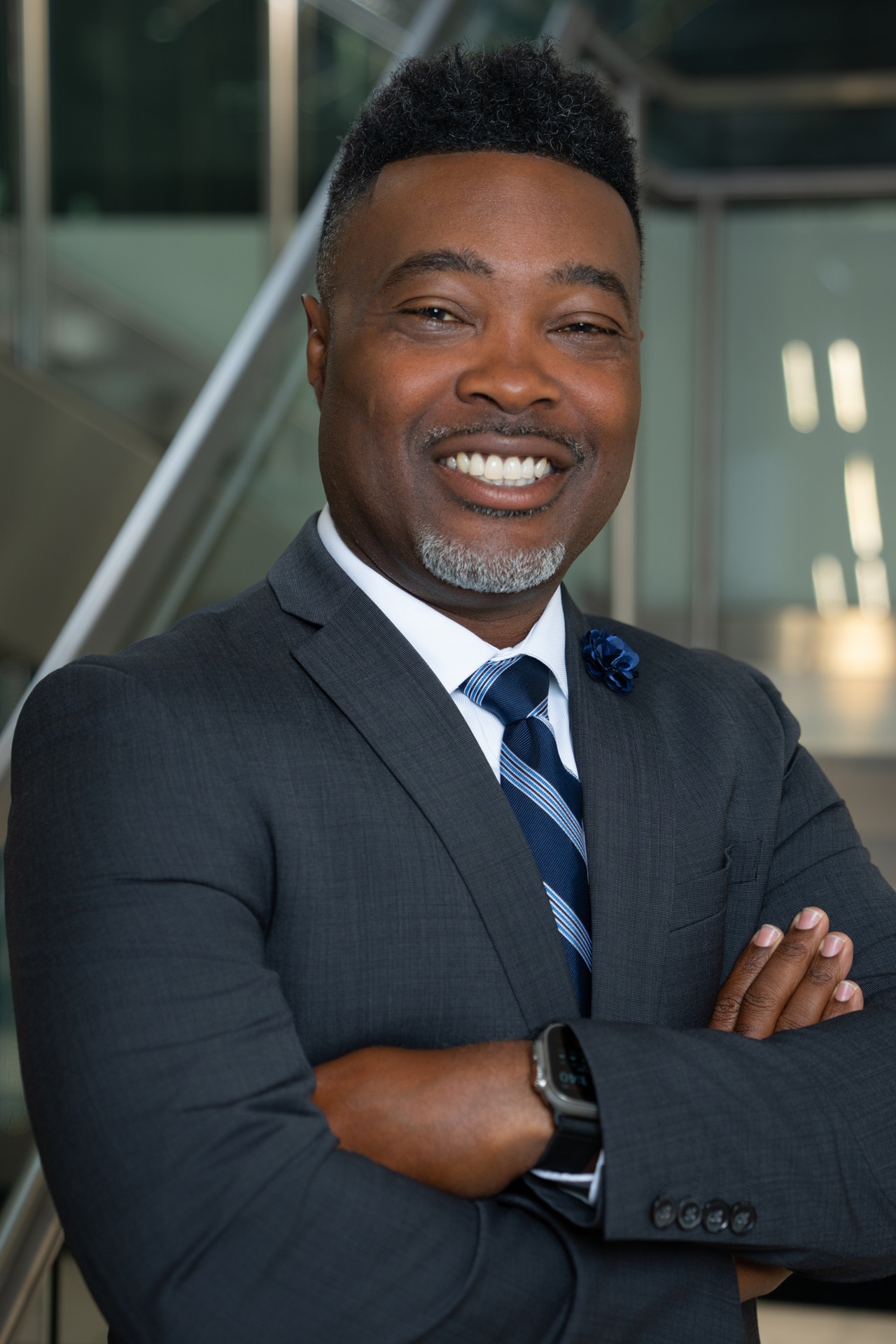 Portrait of Gebre Jennings smiling confidently in a suit with crossed arms.