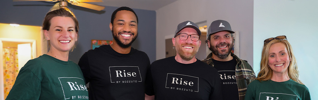 Five smiling individuals wearing Rise shirts in a cozy interior.