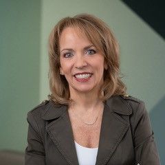 A smiling woman with medium-length brown hair, wearing a dark jacket, against a muted background.