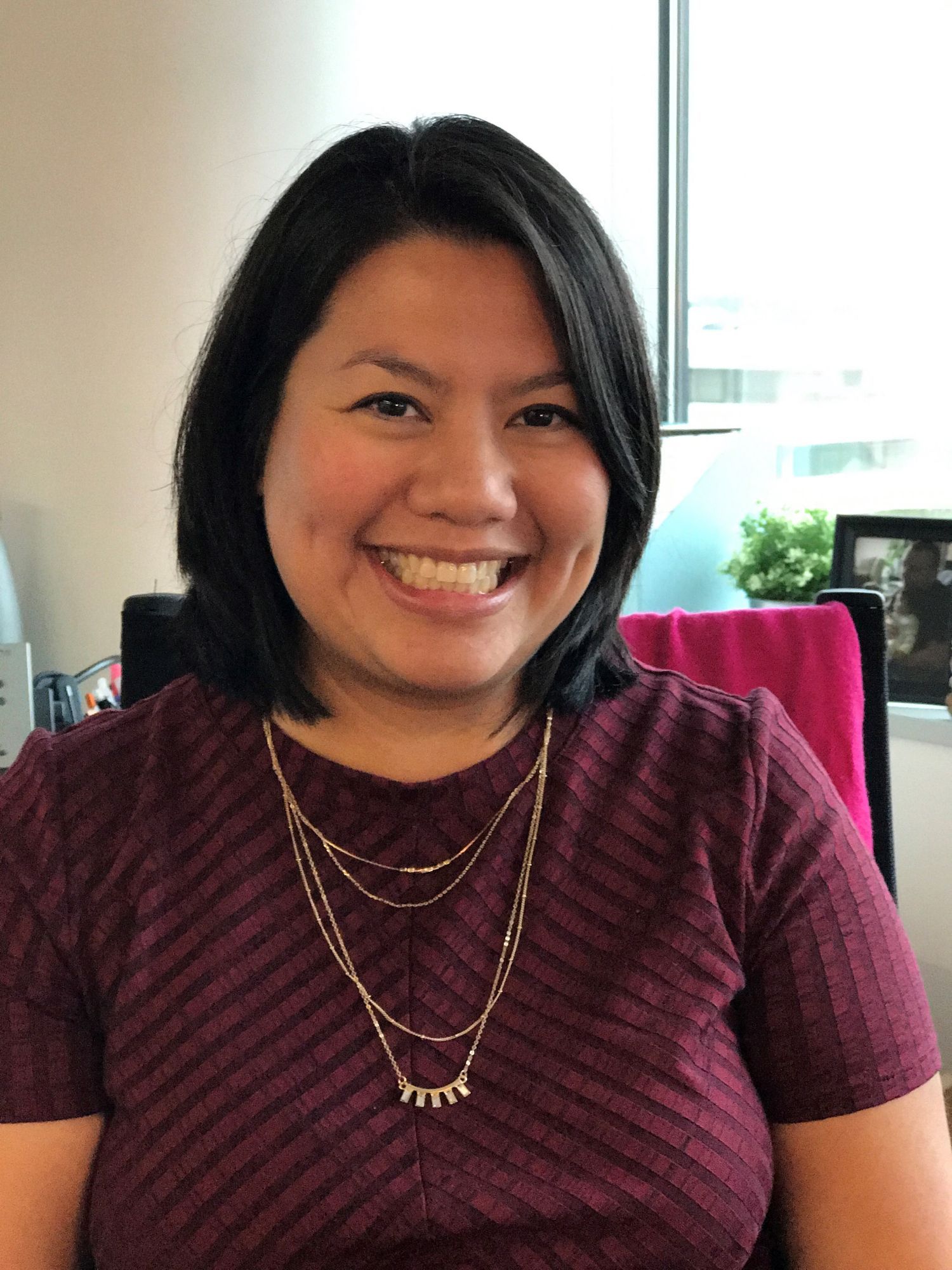 Smiling woman with dark hair, wearing a striped top, seated in an office environment.