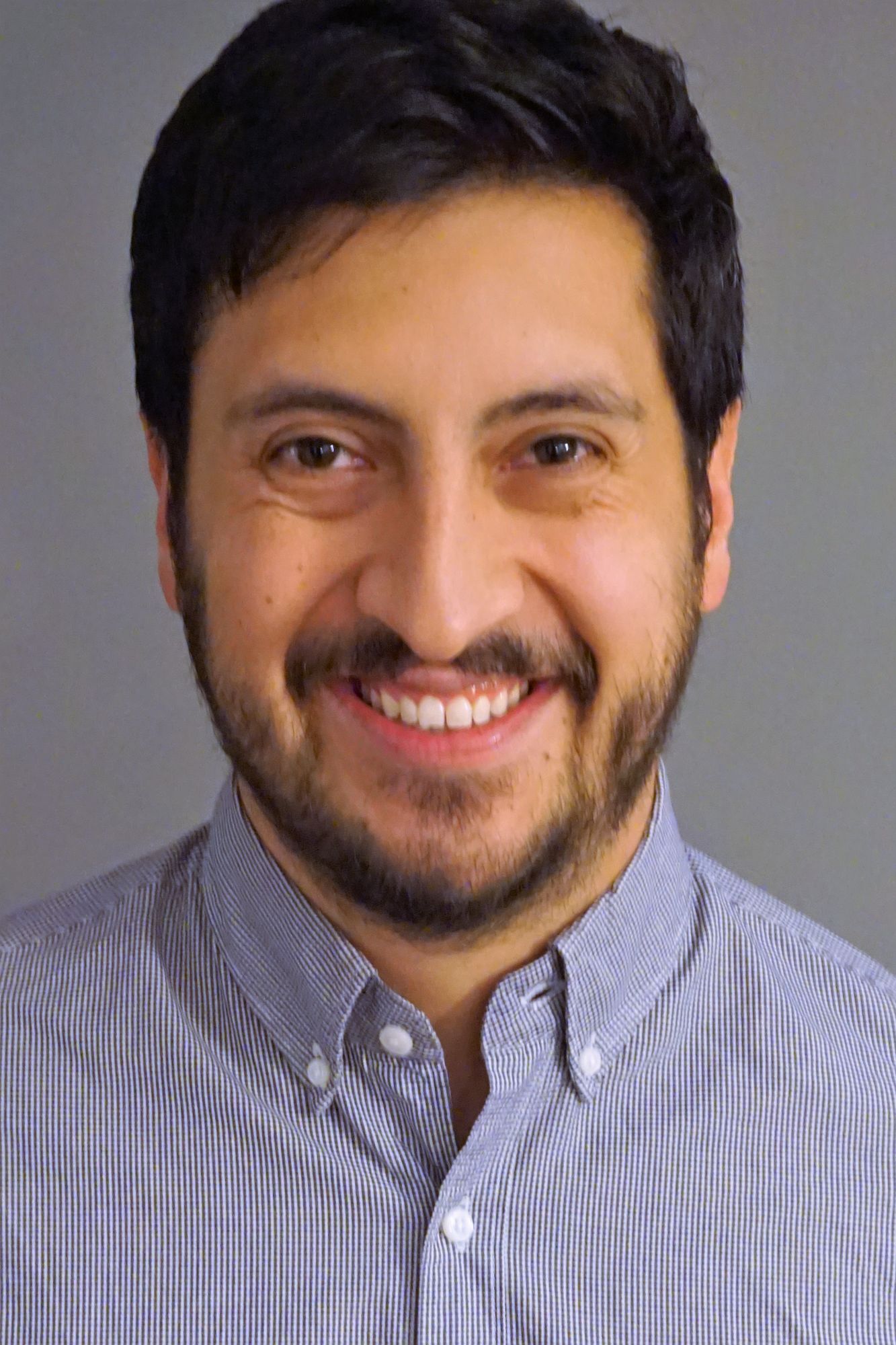 Smiling man with a beard wearing a collared shirt and a neutral background.