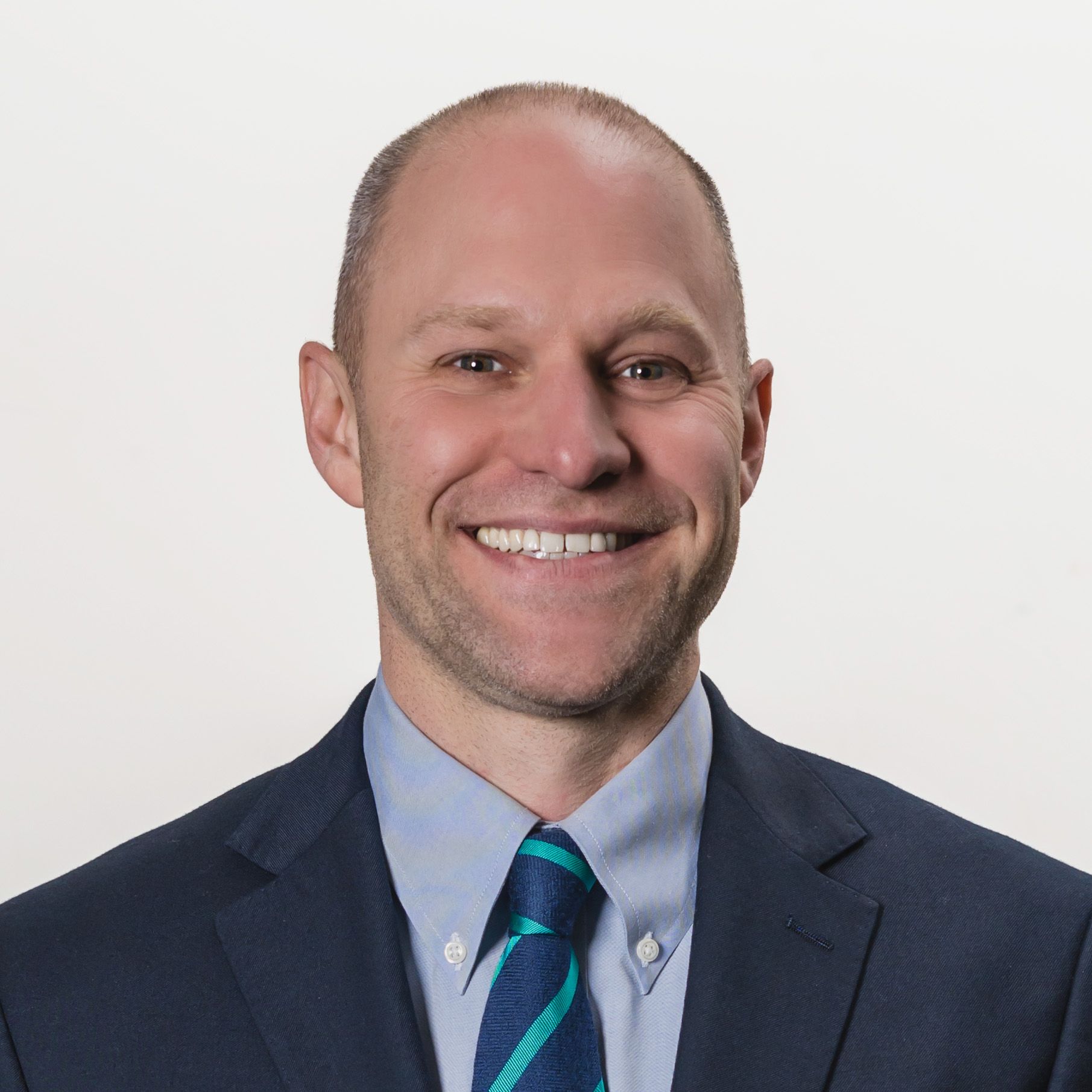 Smiling man in a suit with a tie against a plain background.