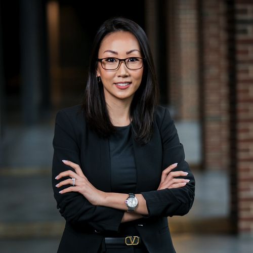 Professional woman in a black blazer and glasses, standing with arms crossed.