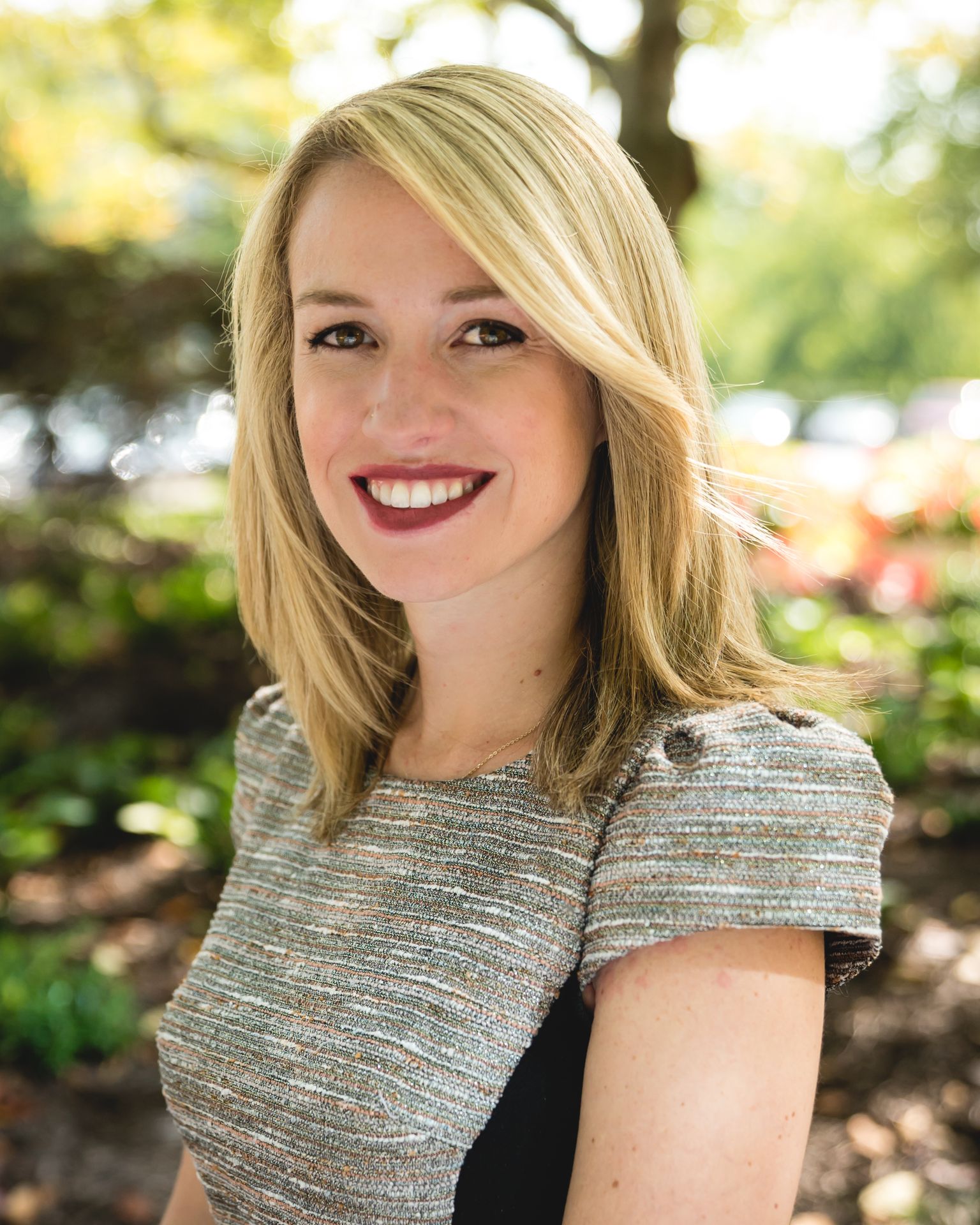 A smiling Jessica Barnes poses outdoors with greenery in the background.