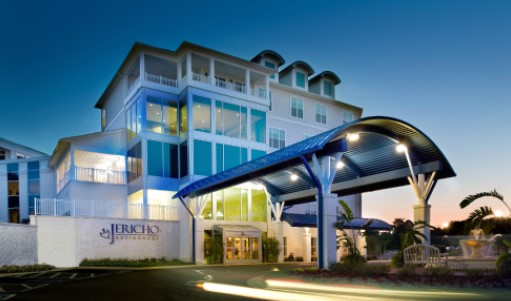 Multi-story senior living community with a coastal-inspired design, featuring white exterior finishes, large windows, and covered balconies.
