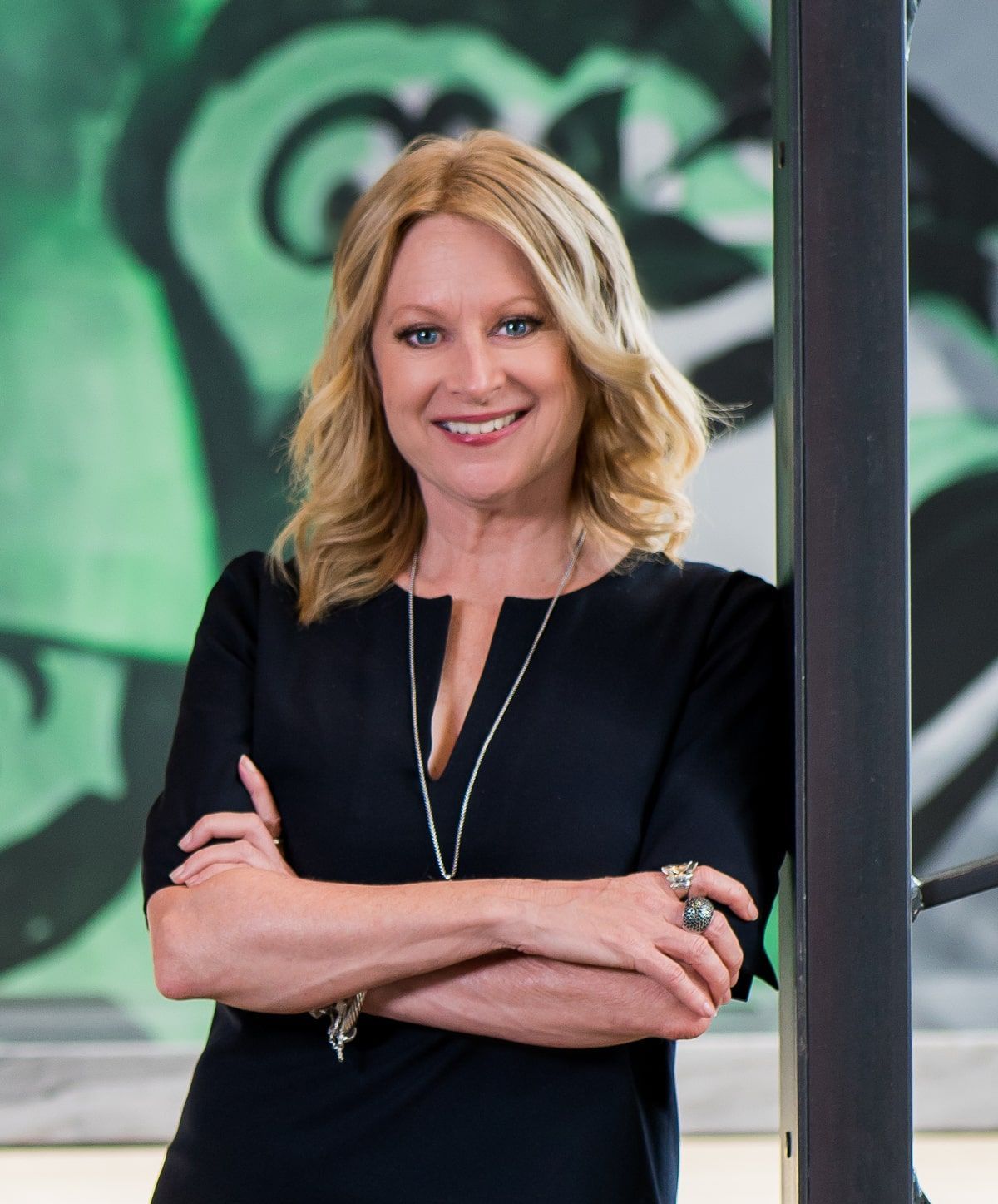 A person with blonde hair smiles confidently, standing against a colorful backdrop.