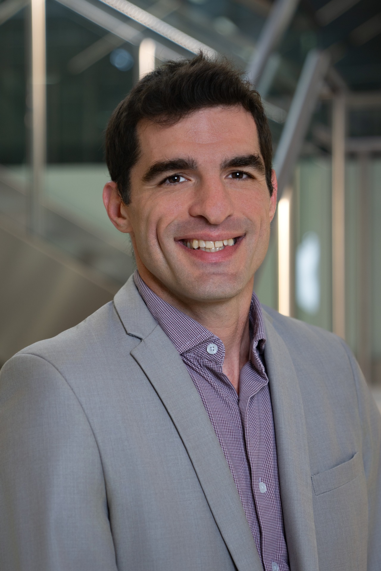 Portrait of Joel Regignano smiling in a light grey suit with a modern background.