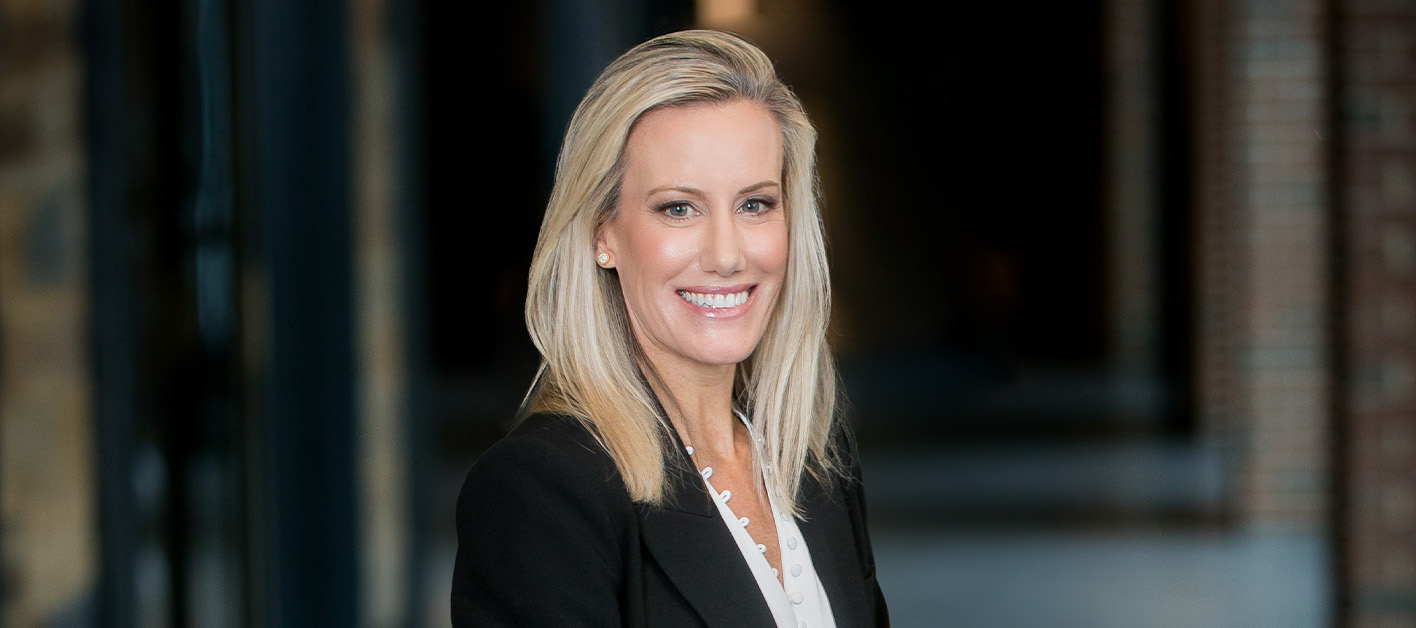 Smiling woman in a black blazer standing indoors.