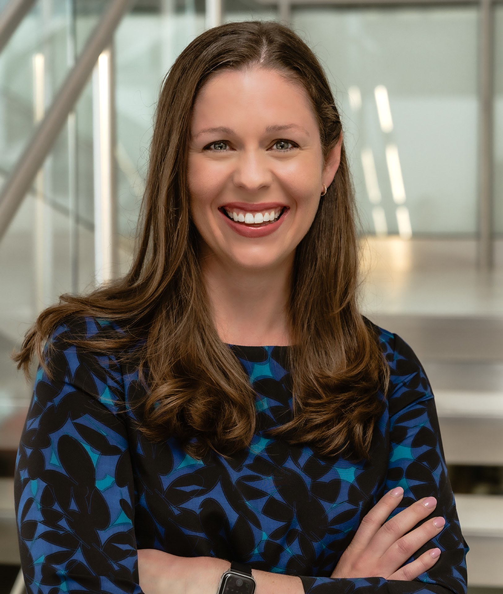 Kate Becker smiles confidently with arms crossed in a modern, bright interior setting.